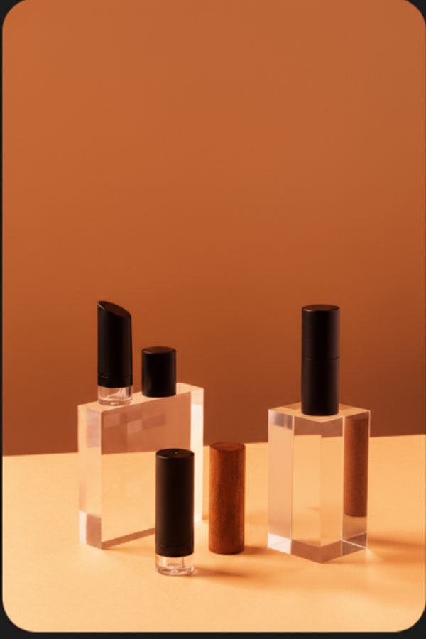 «چند بطری پمپ ایرلس شیشه‌ای شفاف با درب مشکی و درب چوبی، قرار گرفته روی مکعب‌های کریستالی در پس‌زمینه نارنجی»